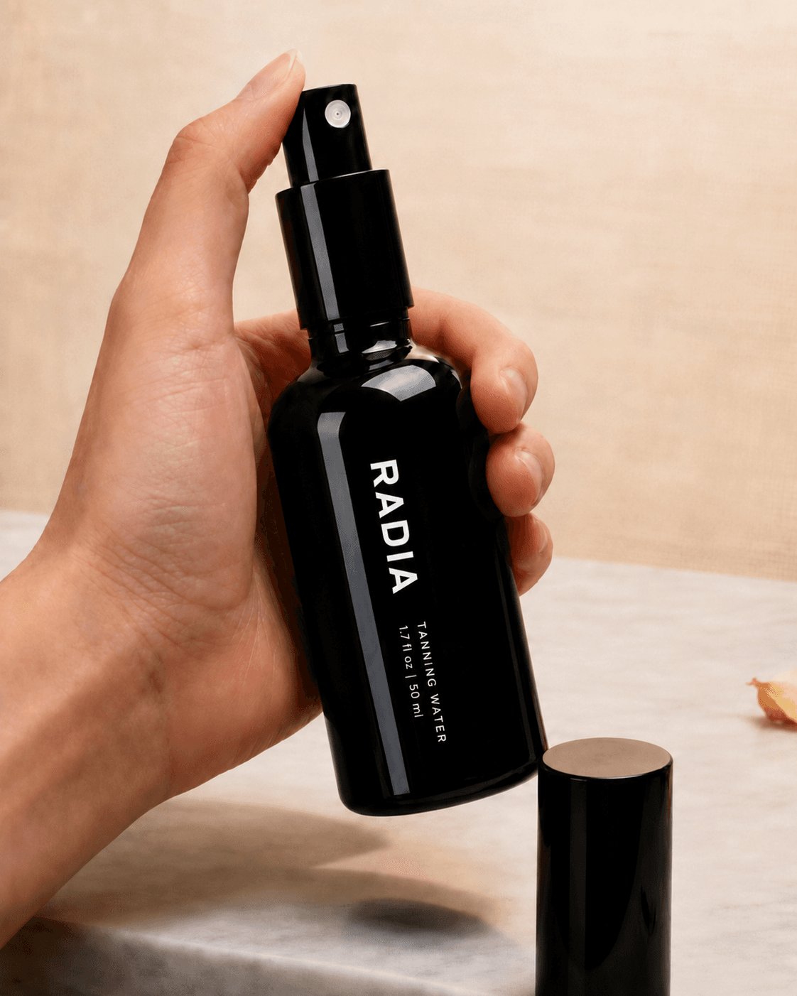A hand holding the black Radia tanning water spray bottle